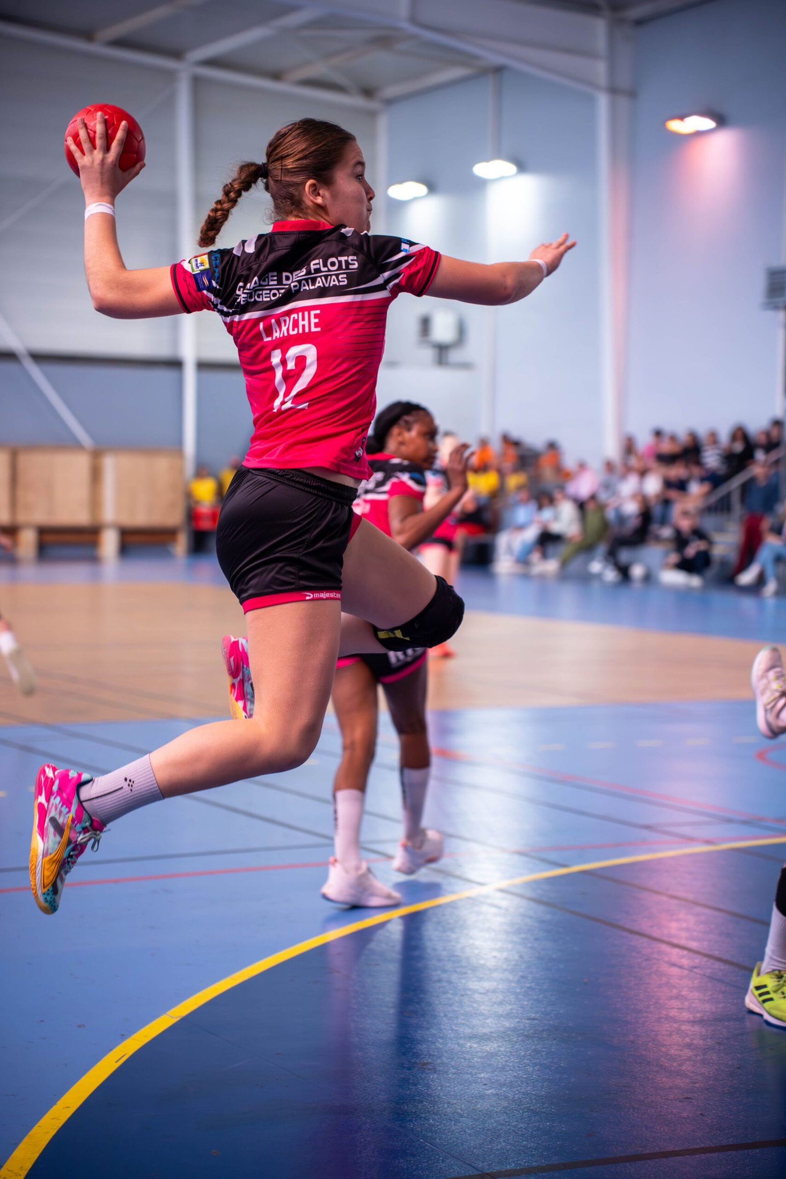 Női kézilabdázó lövésre készül egy sportcsarnokban